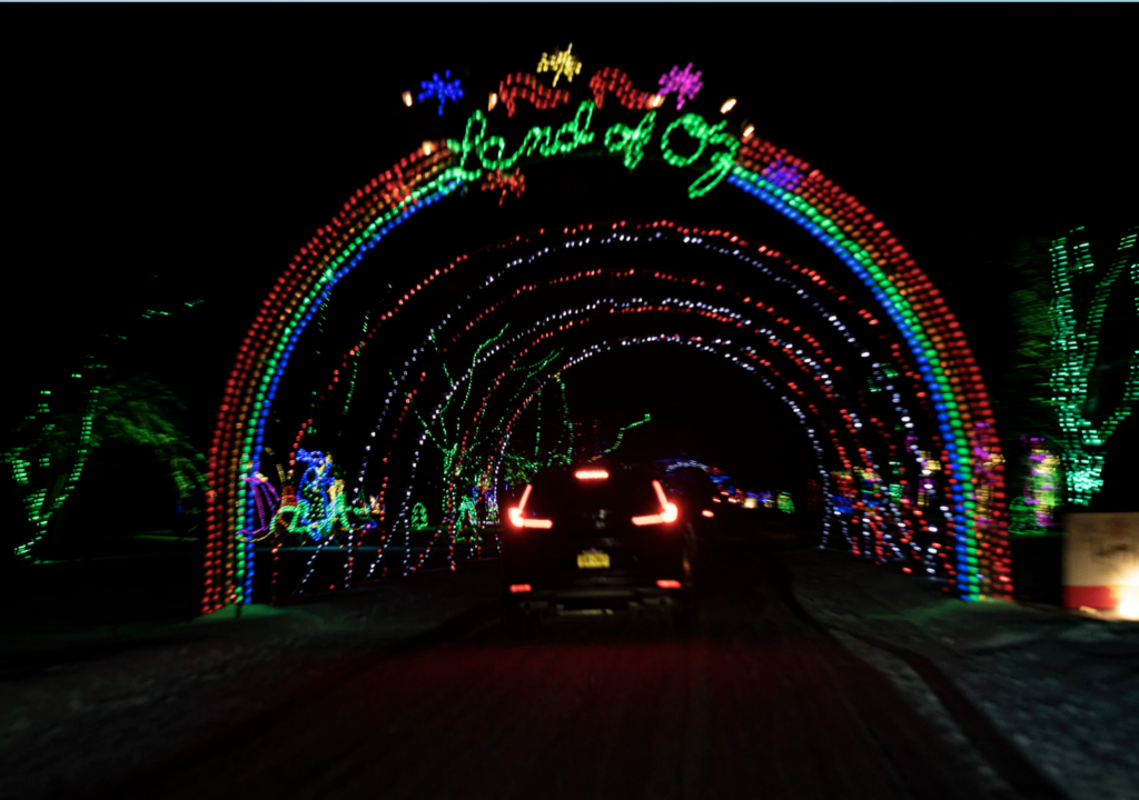 Christmas lights of multiple colors create an archway over a road. 